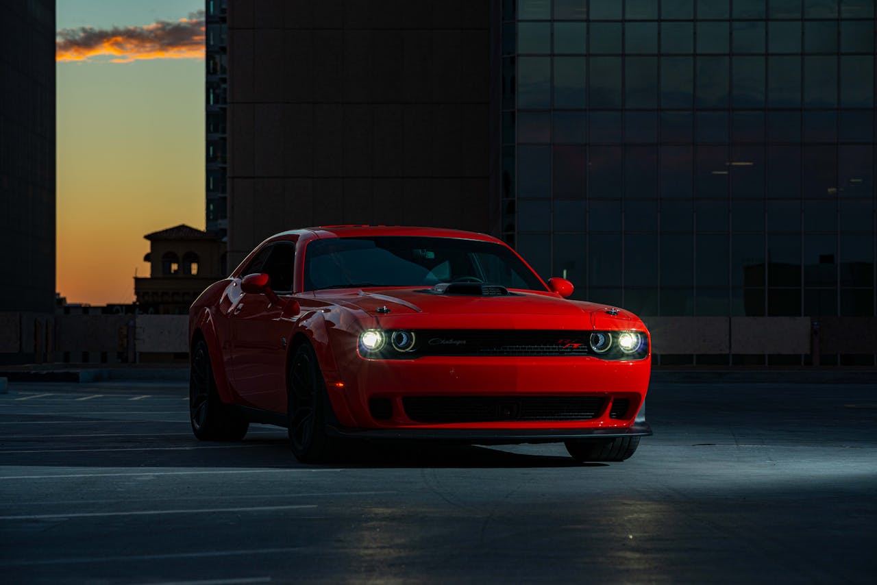 A striking red Dodge Challenger parked outdoors in an urban area at twilight.