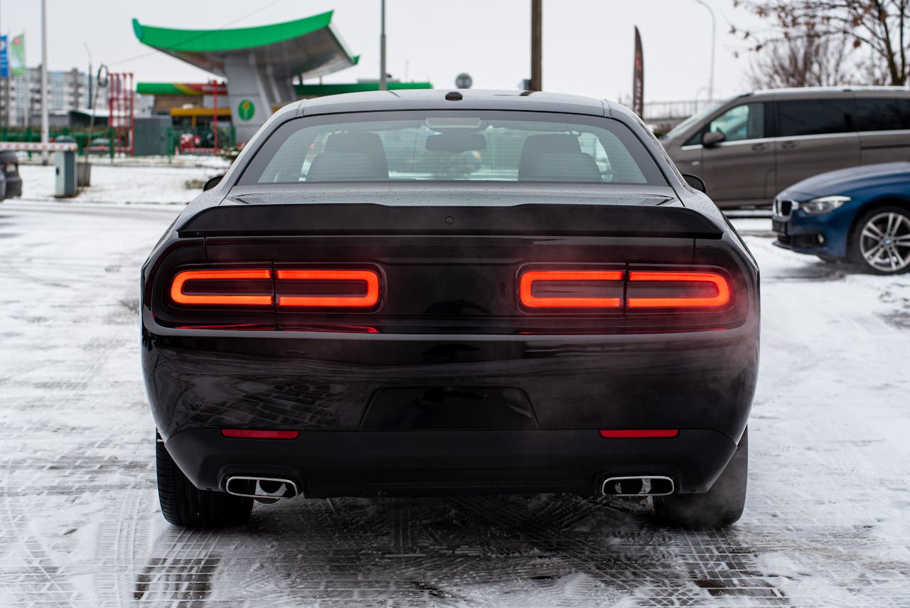 Black luxury car parked on a snow-covered ground at a gas station during winter.