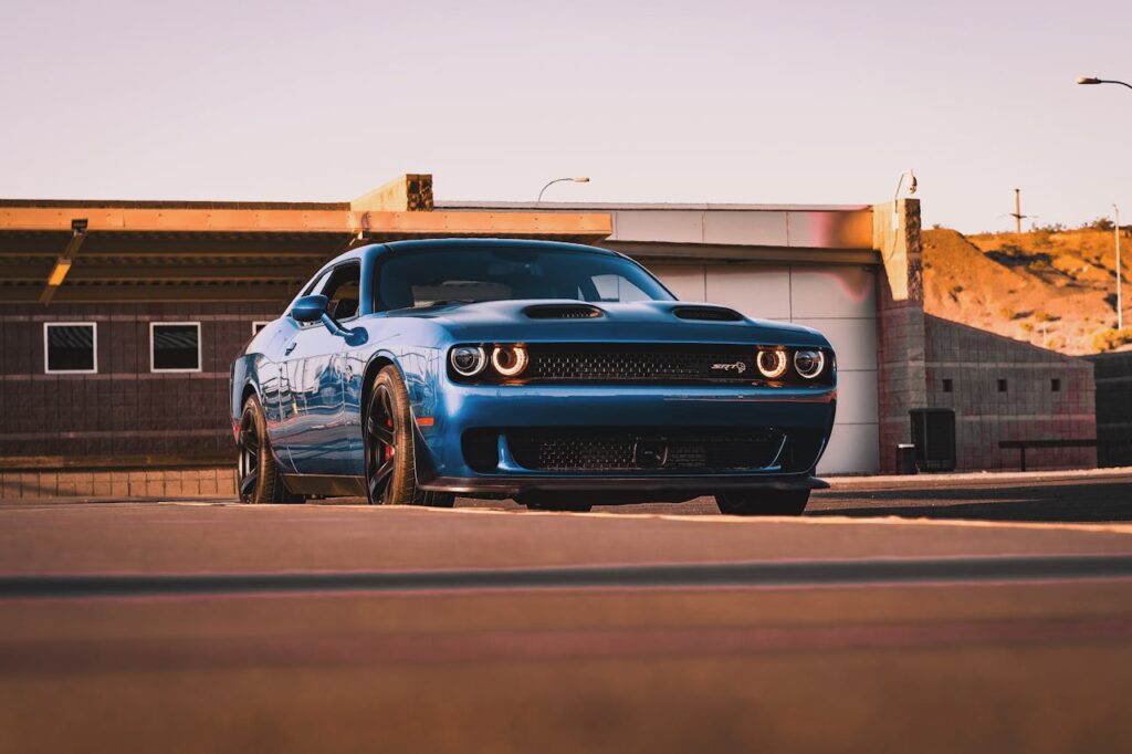 Dynamic shot of a blue Dodge Challenger muscle car in an urban environment during sunset.